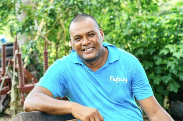 Joseph Hill in a blue shirt sits on a bench, involved in discussions with farmers about resilience to climate change in Fiji.