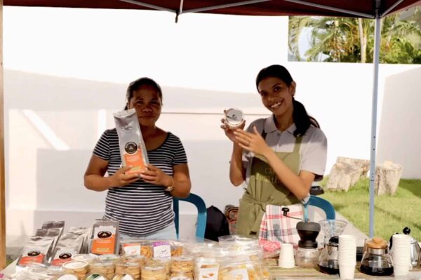 Two young women selling local coffee and produce at a stand during the Festival Kafe Timor in Timor-Leste.