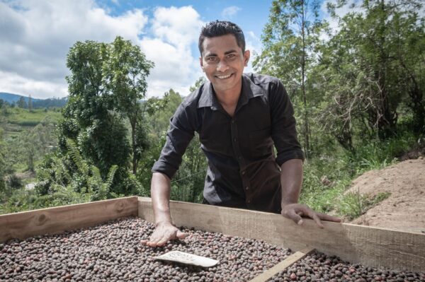A happy man poses next to a table of coffee beans, representing the investment potential in Sri Lankan coffee.