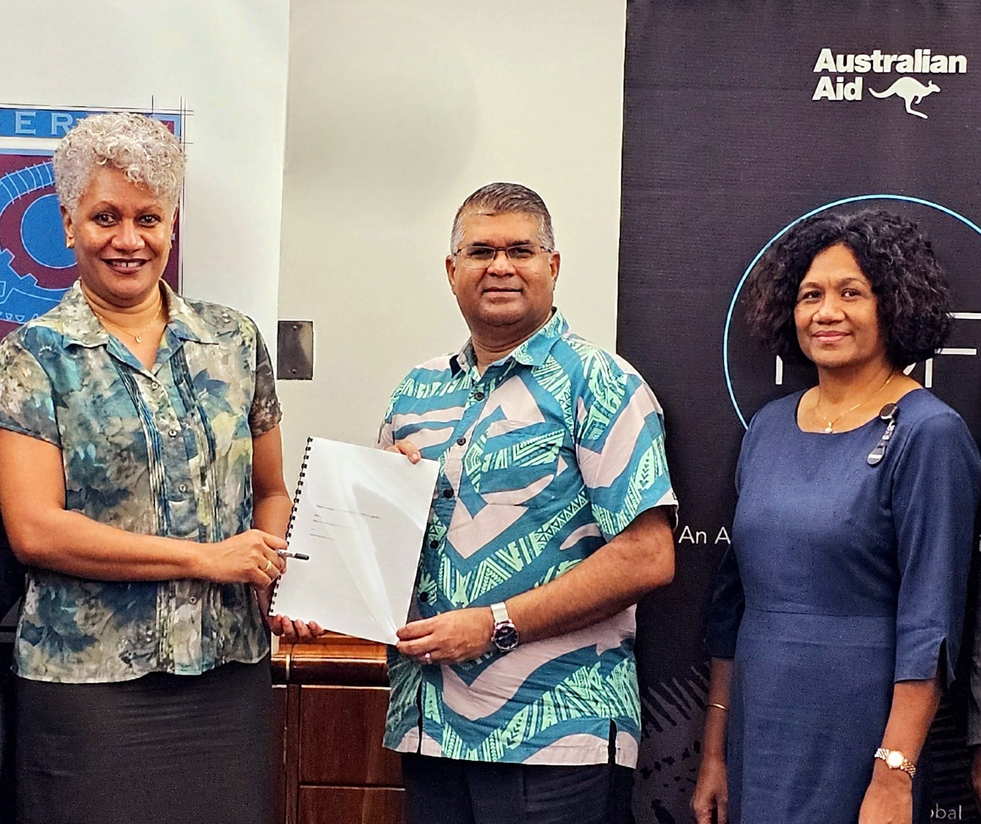 Representatives holding documents beside an Australian Aid banner at an MSME assessment event in Fiji.