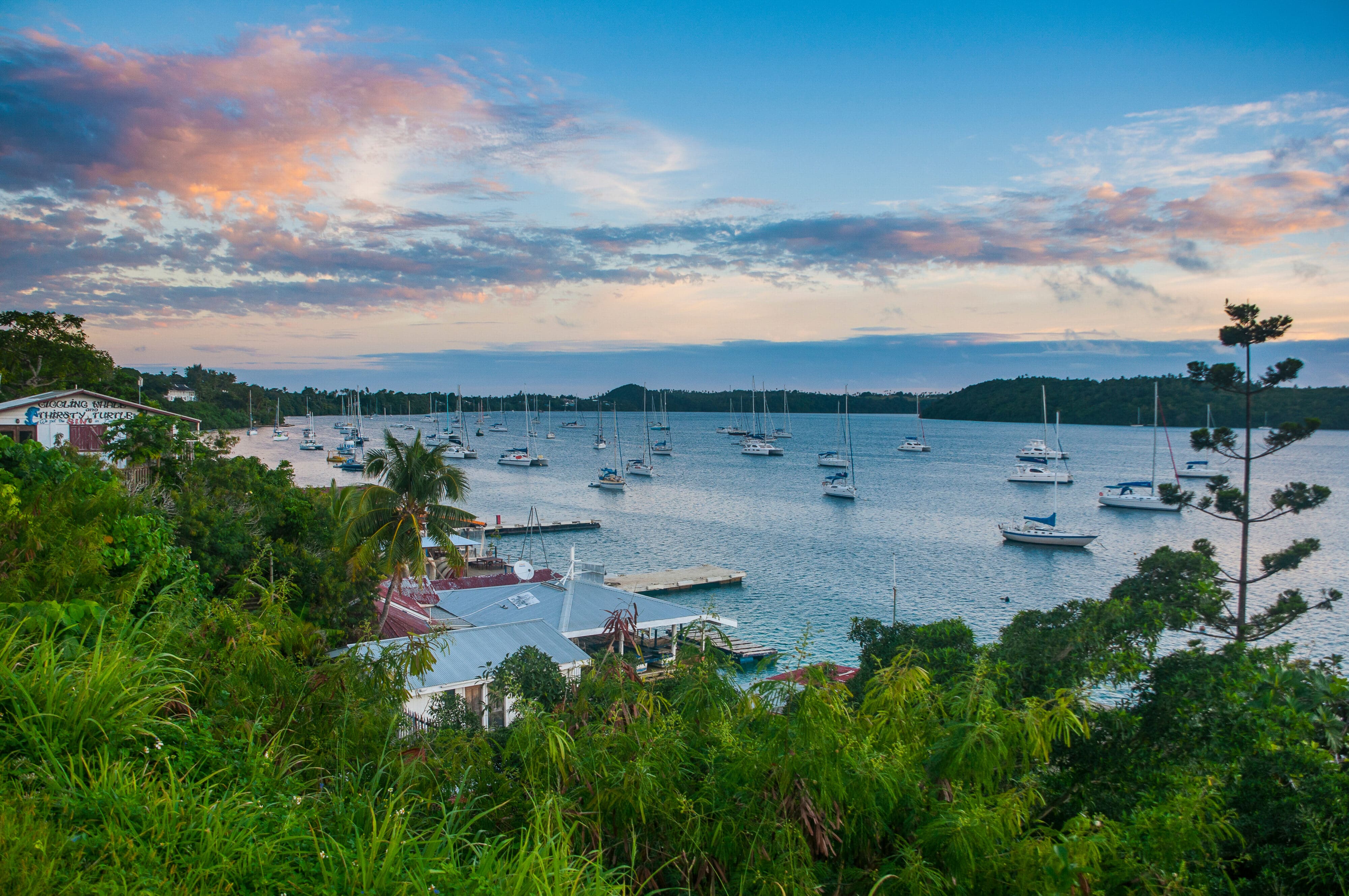 Sailboats anchored in a sheltered bay in Tonga at sunset.
