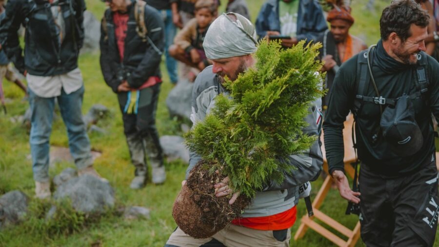 Tour operators and community members gathered outdoors as a man carries a plant.