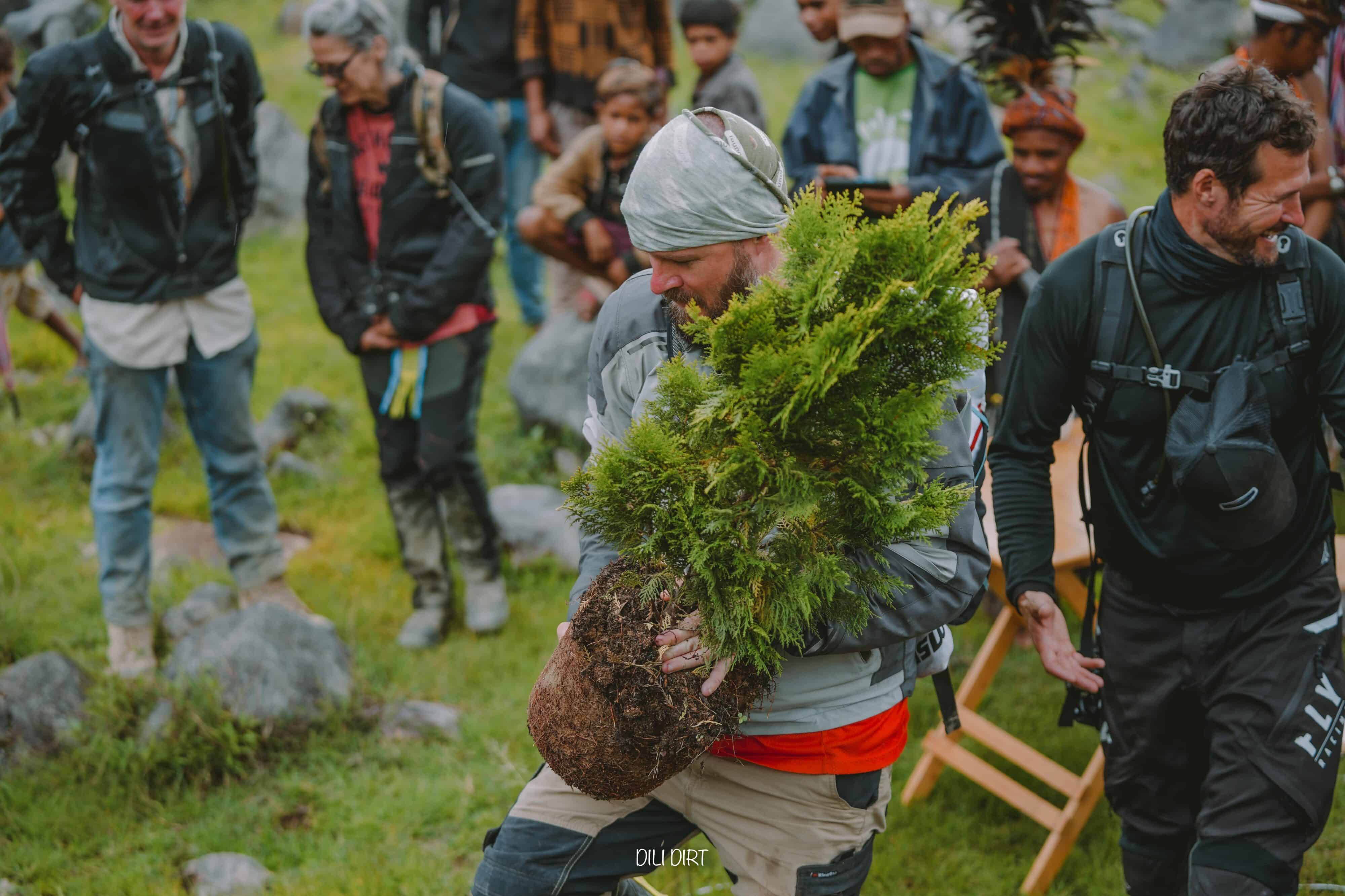 Tour operators and community members gathered outdoors as a man carries a plant.