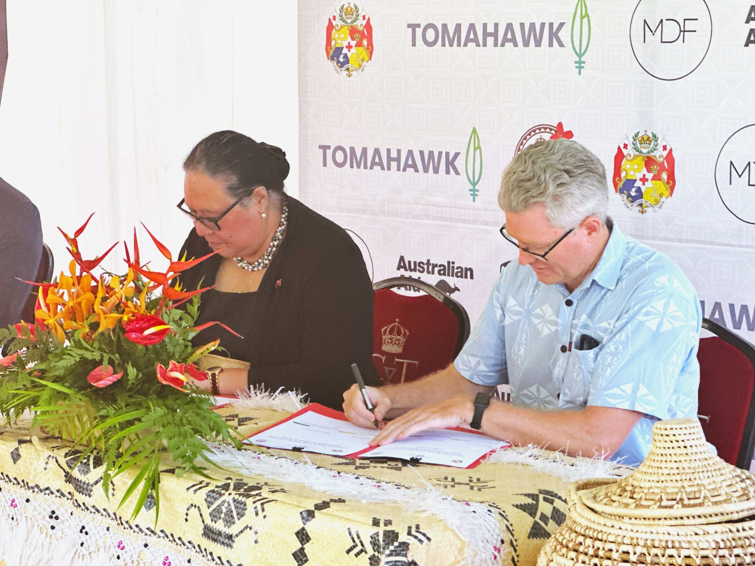 A men and a woman at a table, signing papers for a yacht cruising guide collaboration with Tonga Tourism Authority.