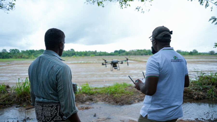 Two men watching a drone fly over a flooded agricultural field in Sri Lanka.
