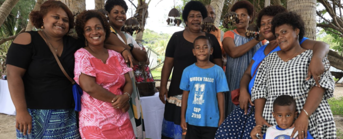 Group of community members smiling under palm trees at a tourism gathering in Fiji.
