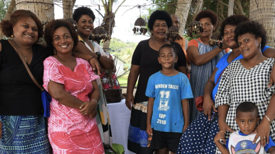 Group of community members smiling under palm trees at a tourism gathering in Fiji.