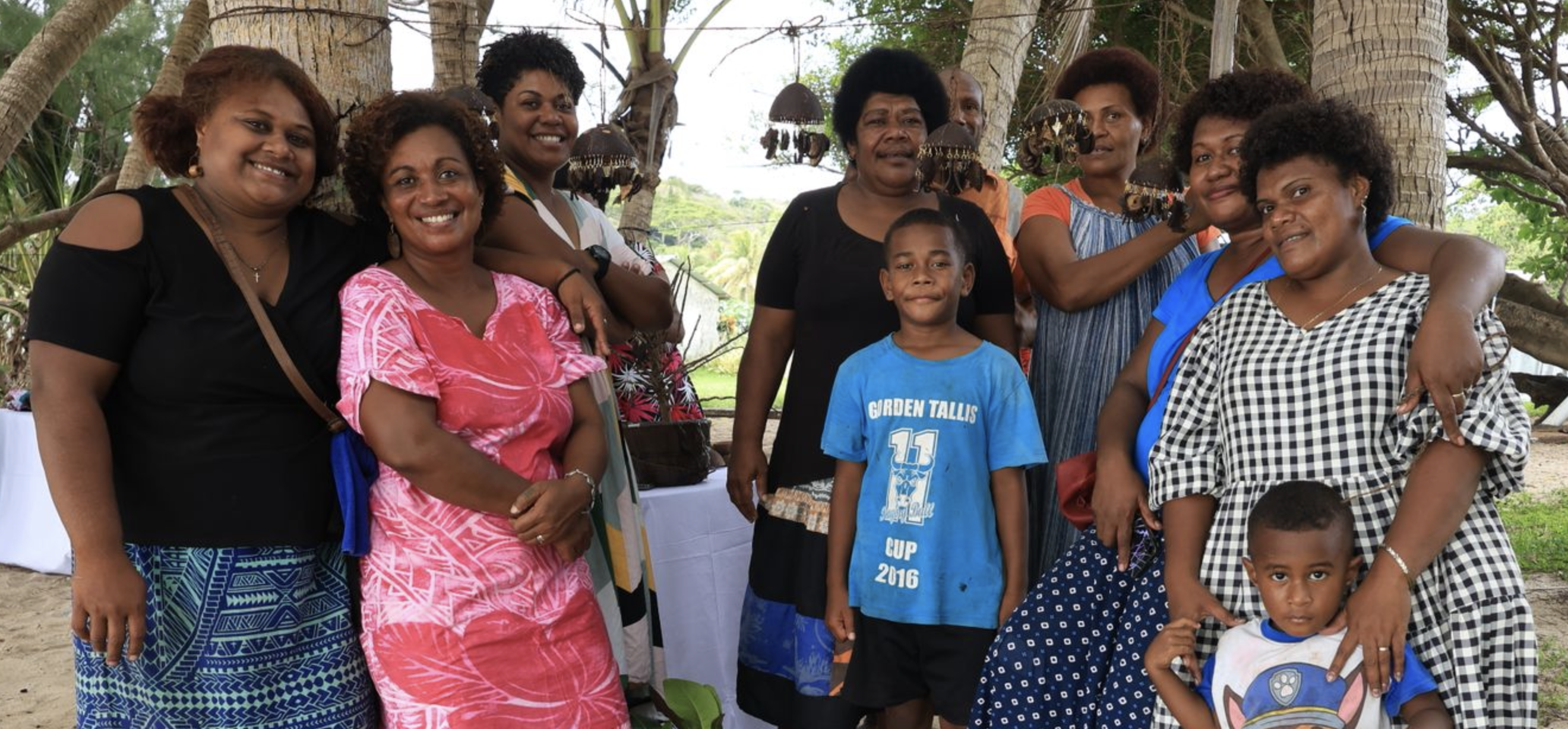 Group of community members smiling under palm trees at a tourism gathering in Fiji.