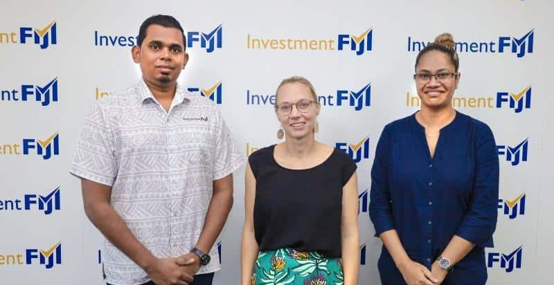 Three professionals stand before an investment Fiji sign, promoting peer-to-peer learning for Australia-Fiji trade investment.