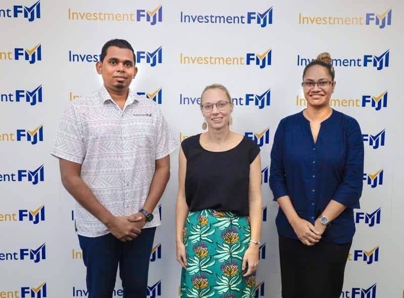 Three professionals stand before an investment Fiji sign, promoting peer-to-peer learning for Australia-Fiji trade investment.