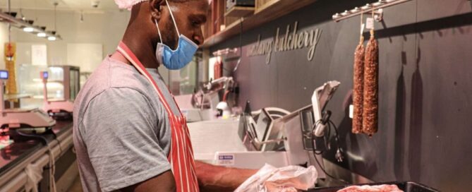 Worker in protective clothing handling meat in a butchery.