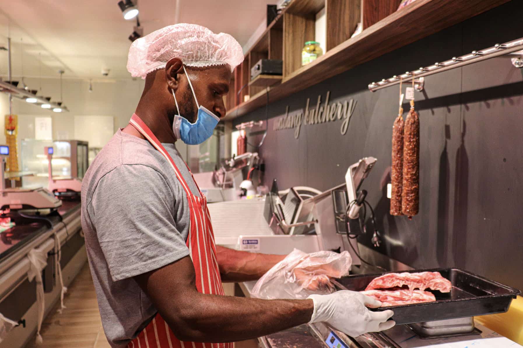 Worker in protective clothing handling meat in a butchery.