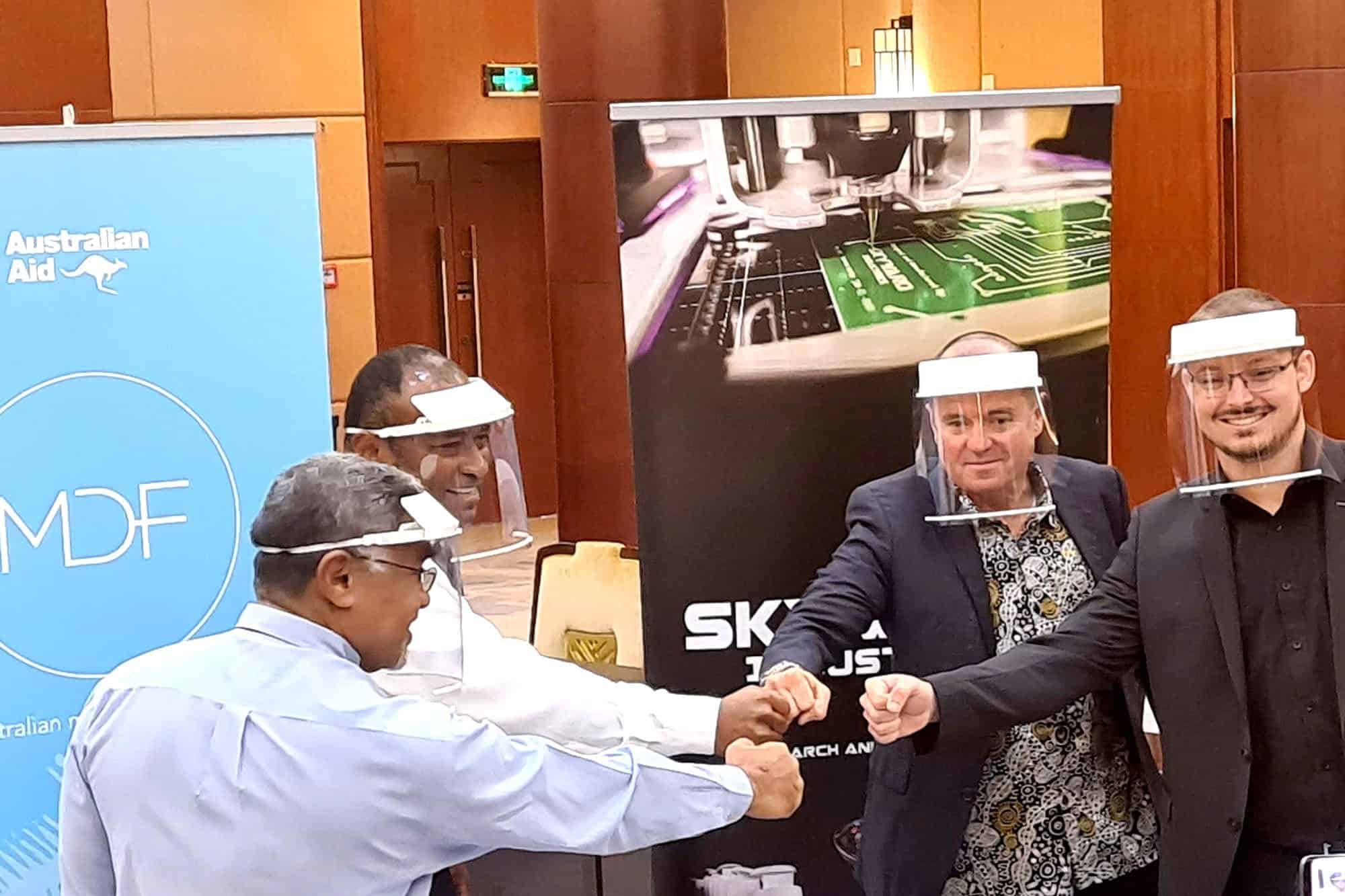 Representatives wearing face shields fist bumping at an MDF handover event in Fiji.