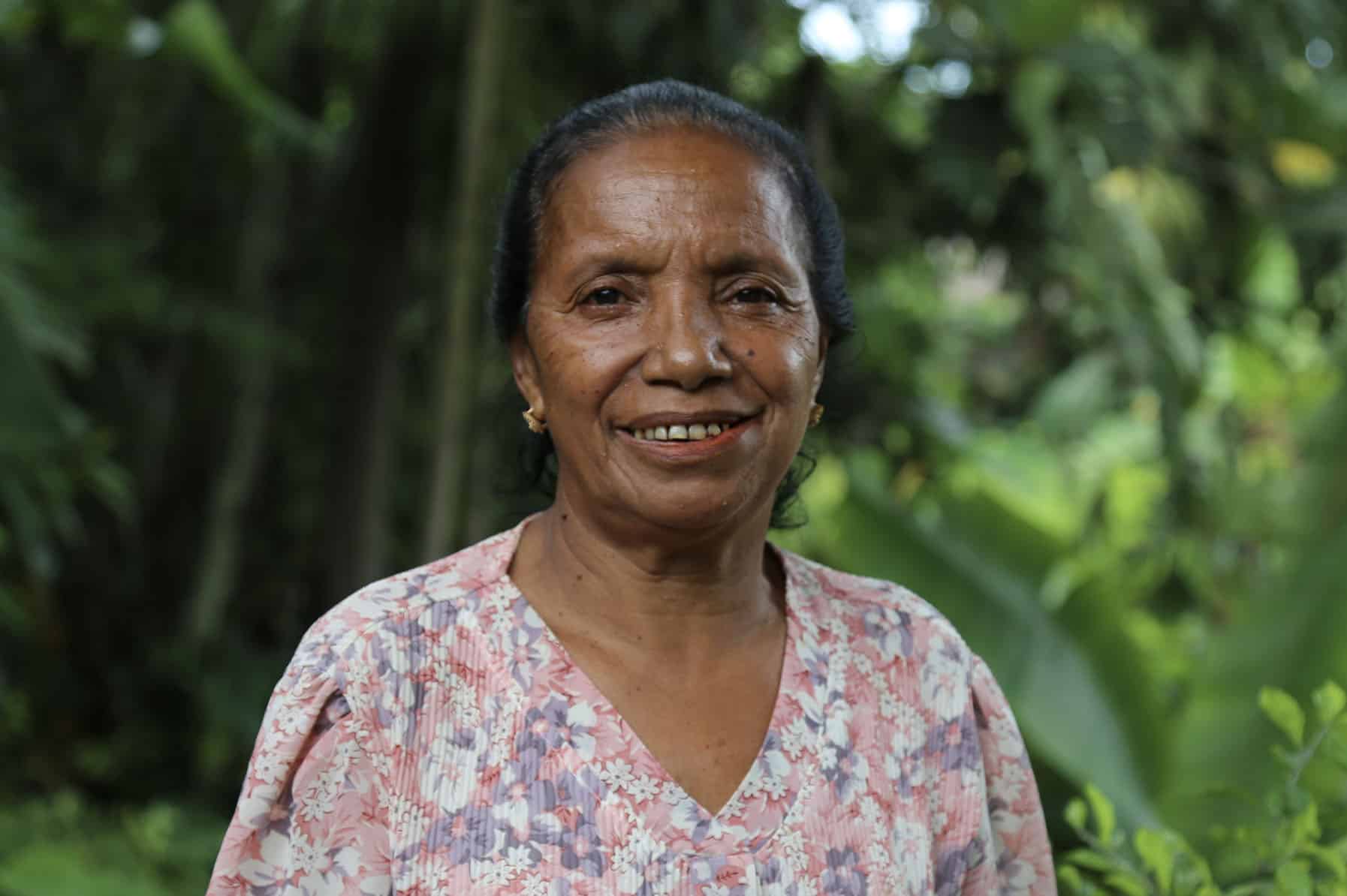 Joana de Sá, an older Timorese’s pig farmer, smiles at the camera, thinking of the benefits of easier feeding practices.