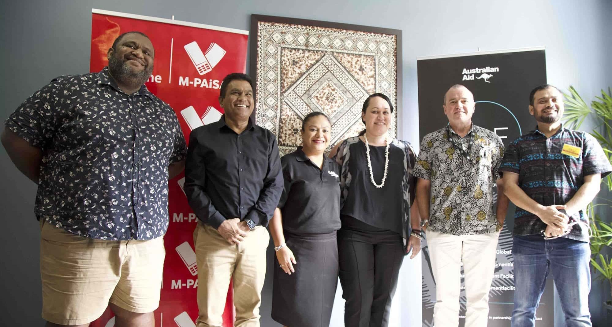 Group of representatives standing together beside M-PAiSA, Australian Aid and MDF banners in Fiji.
