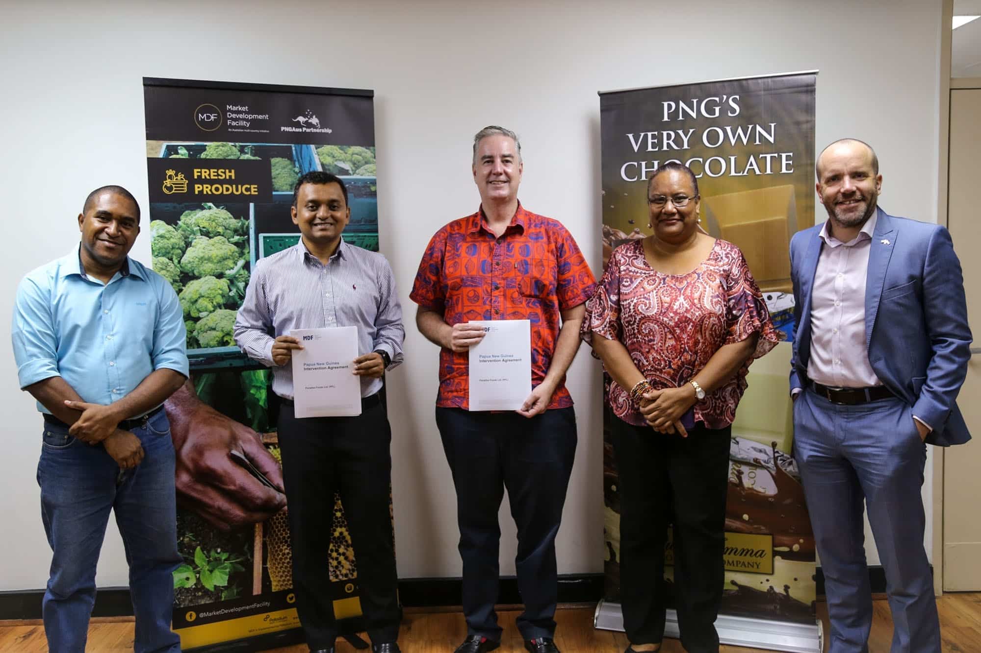 Representatives holding agreement documents beside MDF and Paradise Foods Limited banners in Papua New Guinea.